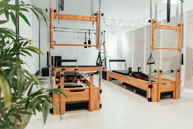 Cover for a yoga vs Pilates comparison: wooden Pilates reformers and tower apparatus in a bright studio.